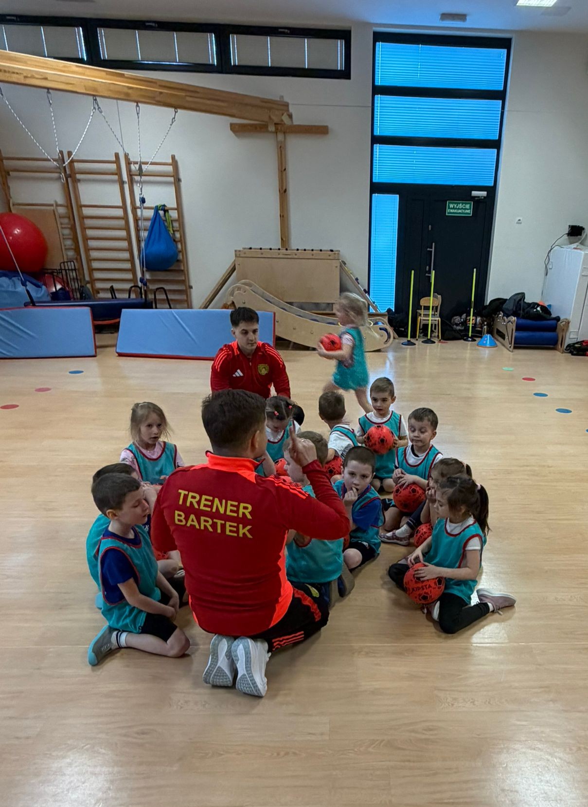 Trener Bartek kucający z piłką i maskotką